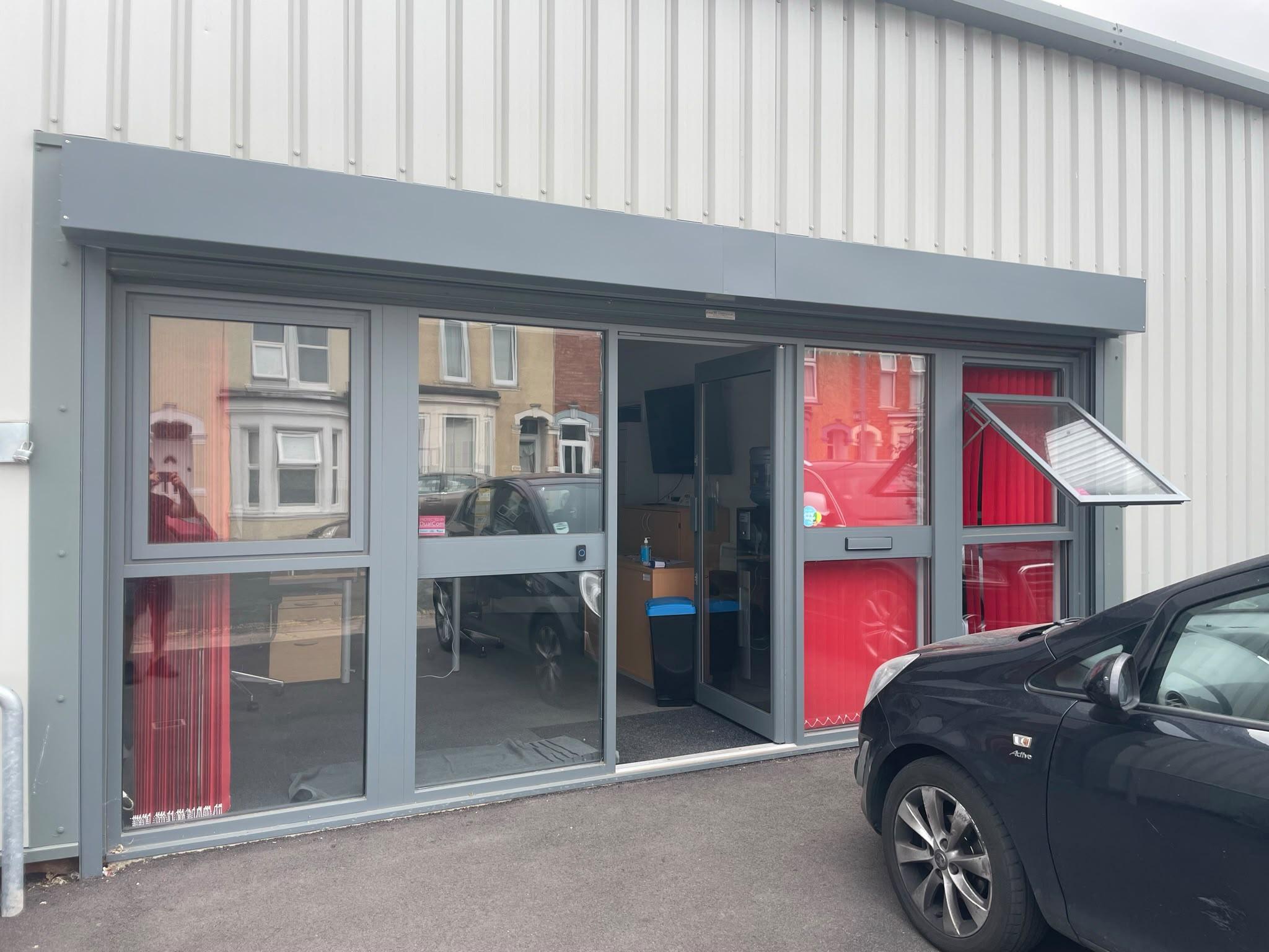 Grey industrial unit office front with clear glass, the office inside visible from the car park