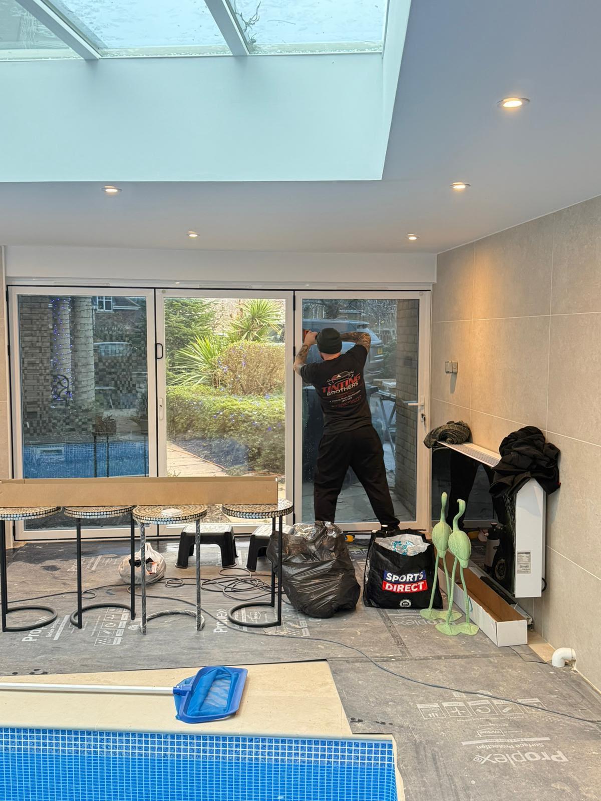 Tinting Brothers fitter applying film to bifold doors in an indoor pool room